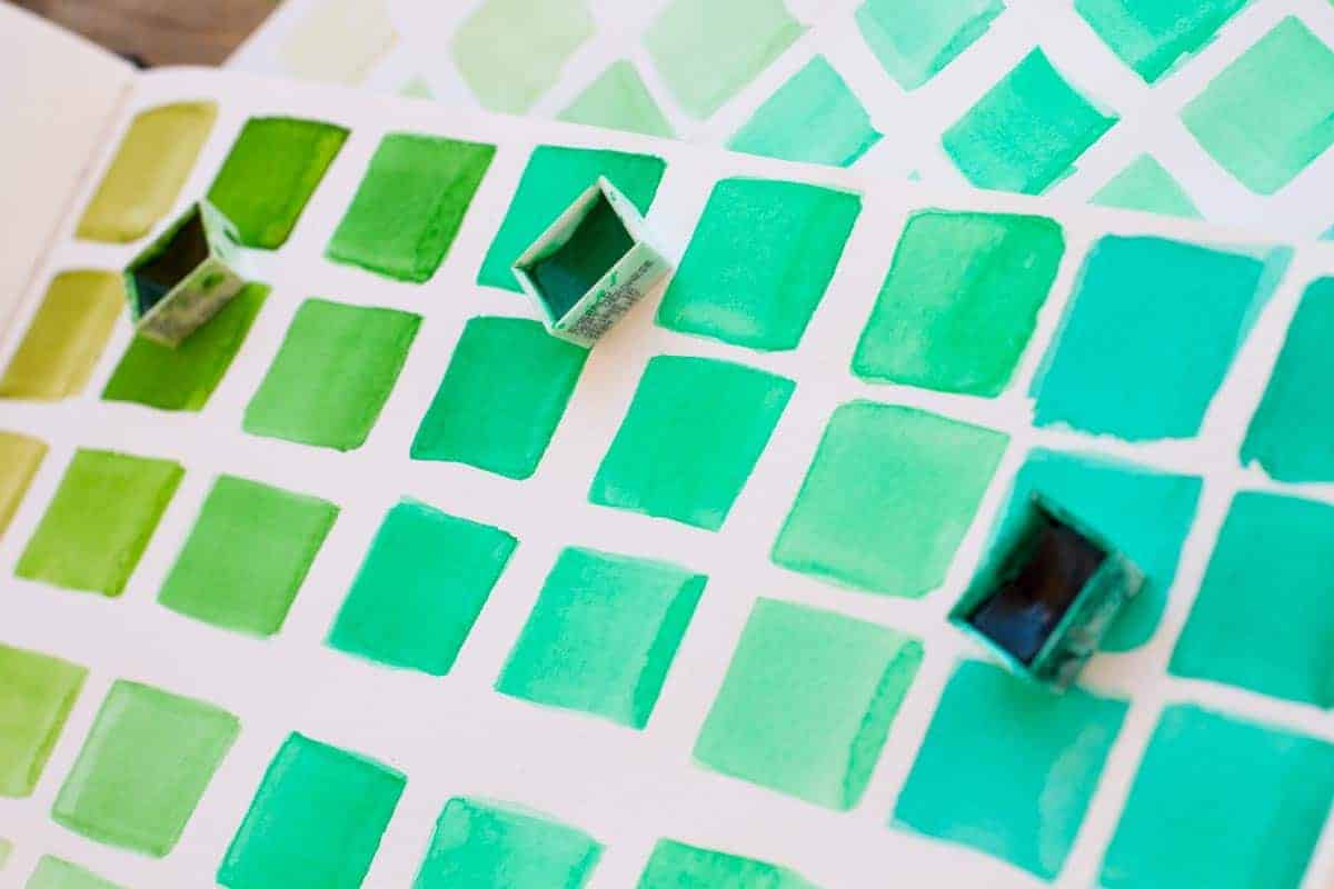 A range of green hues in watercolour paints:  from warm, yellow-based greens to cool, blue-based greens.