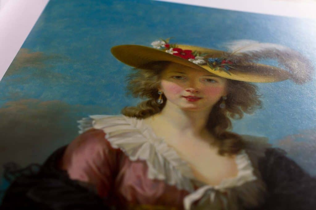 Detail of a painting from the National Gallery exhibition catalogue Rebels and Martyrs, with the 19th century portrait of a woman wearing a wide-brimmed yellow hat with flowers and a large white fluffy feather. By