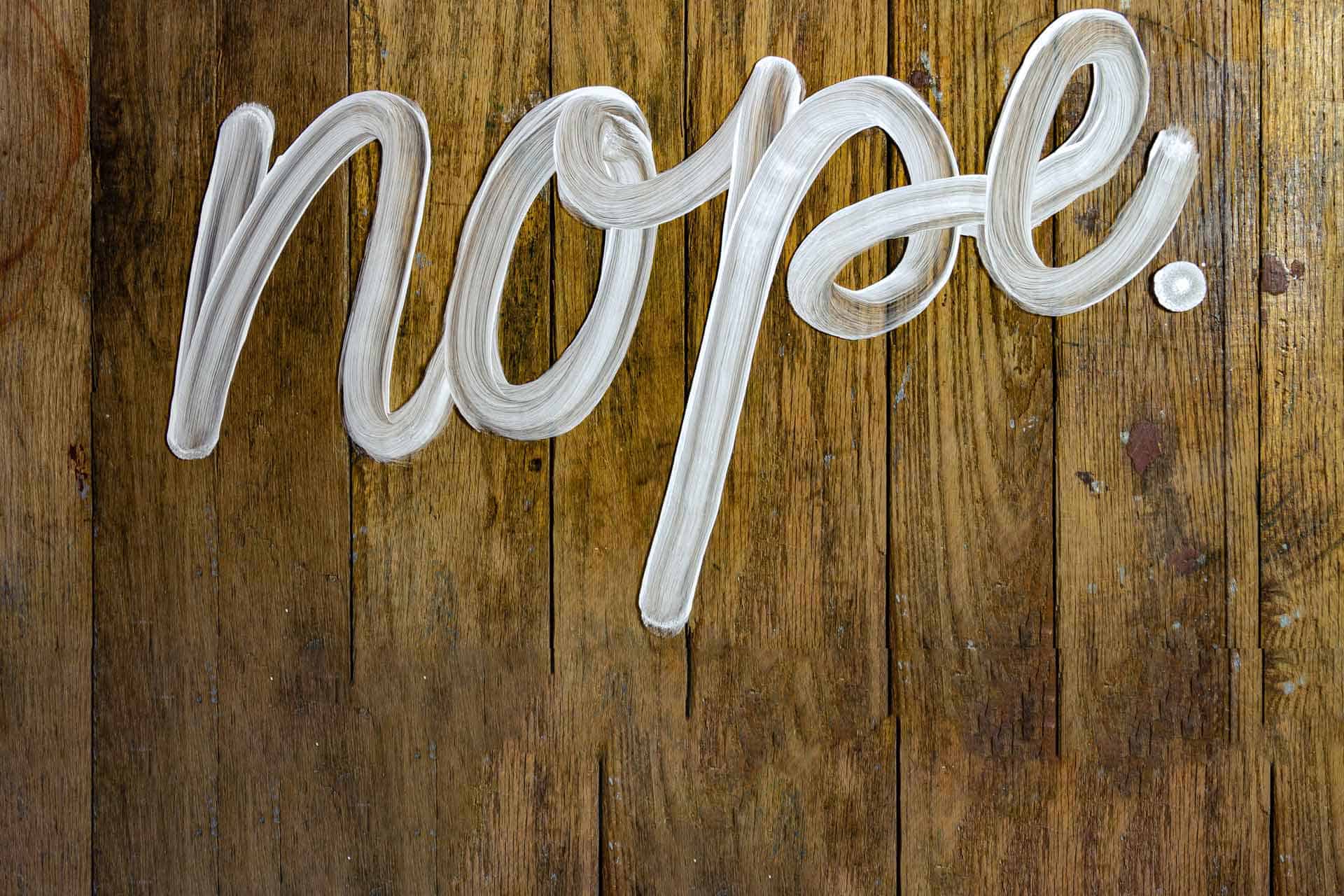 The word "nope" written in white paint against a wooden background. No place for typography mistakes!