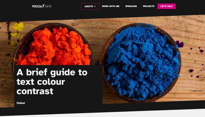 The header of an article on this website, titled A brief guide to text colour contrast. The title is in white text inside a black box, sitting on top of the background image: two small dishes on a wooden table, one full of orange pigment and the other of blue pigment. Both image and copy are visible, but the text is more important than the image. 